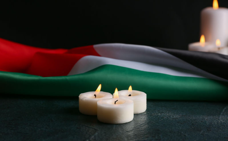 Flag of Palestine and burning candles on black background. Image: Alamy. Contributor: Pixel-shot. Image ID:2XR49MT The real death toll in Gaza