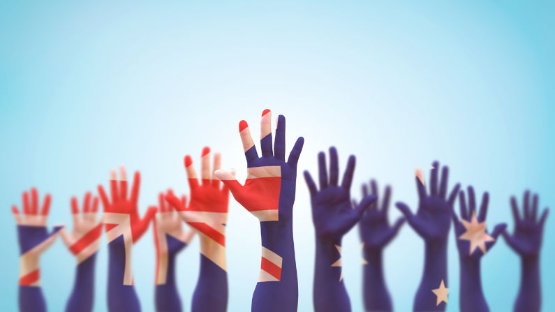 Australian democratic election vote concept with national flag on people open palm hands raising in the air isolated on blue sky background. Image: iStock / Chinnapong Addressing our wicked problems
