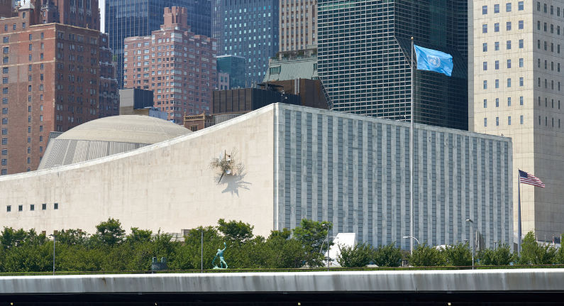 New York, The United Nations General Assembly Building at UN Headquarters in East Midtown Manhattan, NYC. The building is seen from the East River. The UN Flag flies next to the building and sculptures from the UN Collection can be seen. UNGA: Move September meeting to Geneva to allow Palestinians to participate