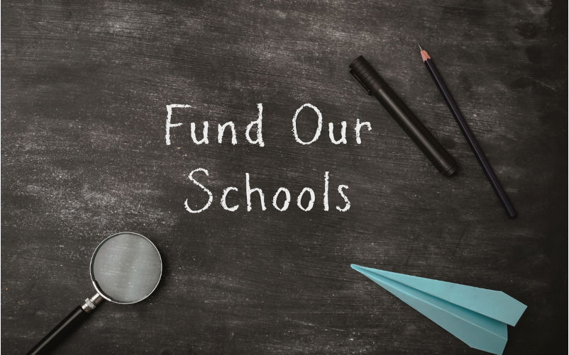 A chalkboard with a magnifying glass, pencils, and a paper airplane. The chalkboard says fund Our Schools. Image iStock / CreditAlla Morozova New school funding agreements deny full funding for public schools
