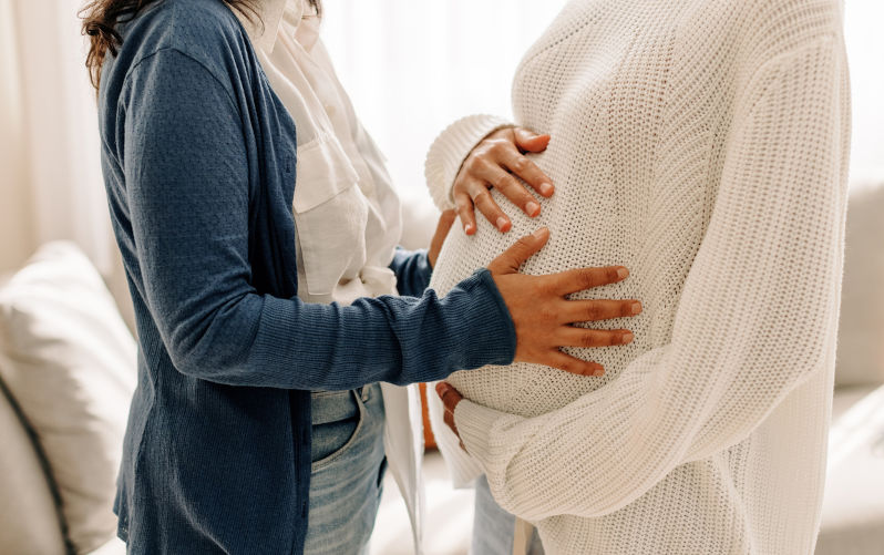 Young woman touching a surrogate mother's belly bump. Young woman spending time with her surrogate at home. Woman feeling the movement of a pregnant woman's baby. Image:iStock/JLco-Julia-Amaral Should Australia legalise commercial surrogacy?