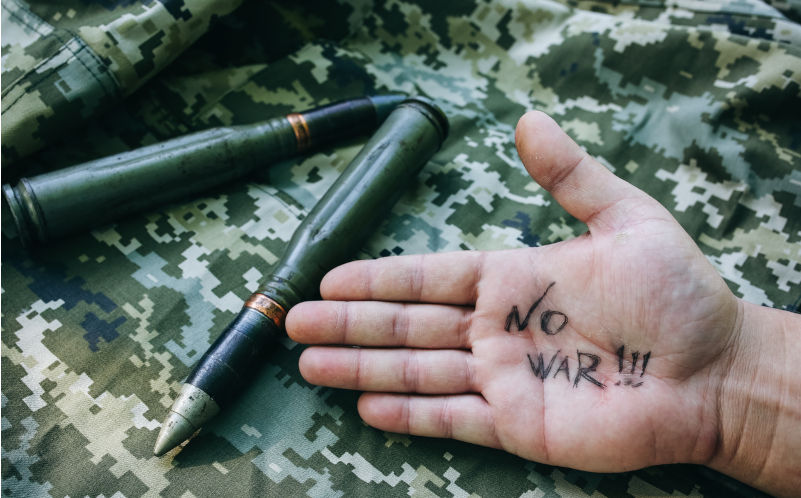 No war sign written on hand. Shell missile is lying on the old khaki jacket. Historical things on armoured fighting vehicle. Image: iStock / Vadym Plysiuk Sustaining hope when war is normalised
