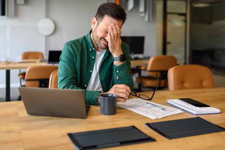 Disappointed young businessman with head in hand sitting with laptop and glasses at desk in office. Image iStock credit Moon Safari Five charts that show how young Australians are getting screwed