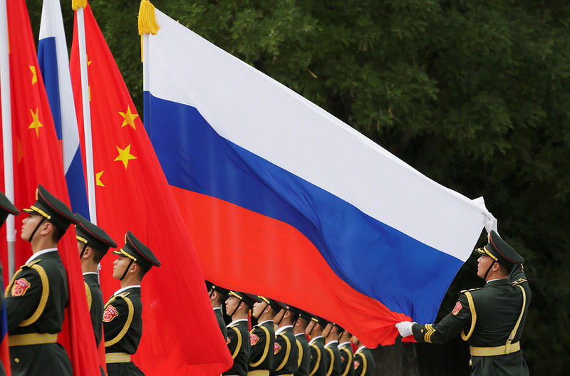 A military officer adjusts a Russian flag ahead of a welcome ceremony hosted by Chinese President Xi Jinping for Russian President Vladimir Putin , 2018