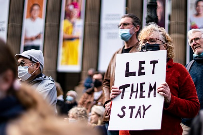 Woman holds a placard saying Let Them Stay at a rally in Melbourne in 2021