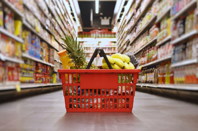 A full grocery basket on the floor of a supermarket aisle