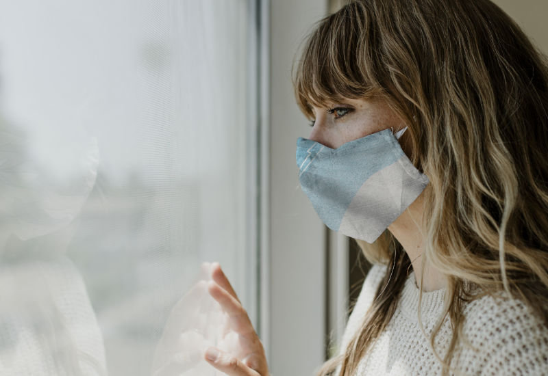 Woman wearing a mask staring out the window during a lockdown