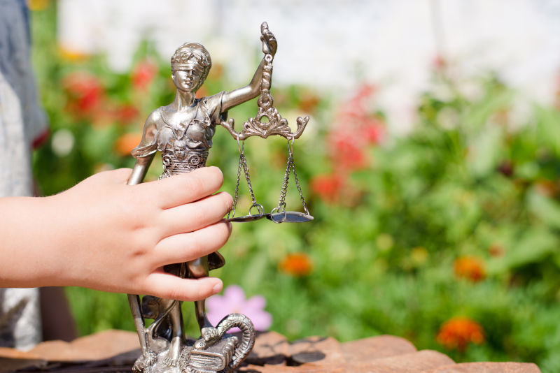 Kid's hand holding sculpture of themis, femida or justice goddess on green leaves natural bokeh background