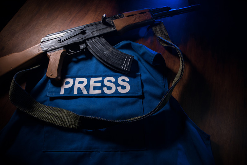 Media Journalism at risk concept. Blue journalist (press) vest in dark with backlight and fog. Weapon on journalist vest.