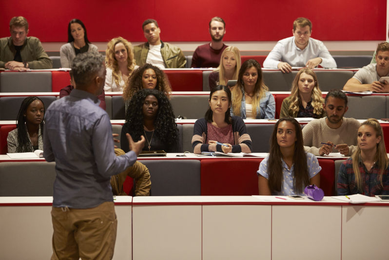 Back-view-of-man-presenting-to -tudents-at-a -lecture Back view of man presenting to students at a lecture theatre