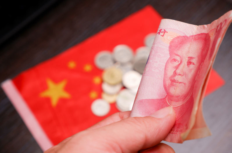 RMB banknotes of Chinese yuan money on the hand with a coins and China flag blurred on background