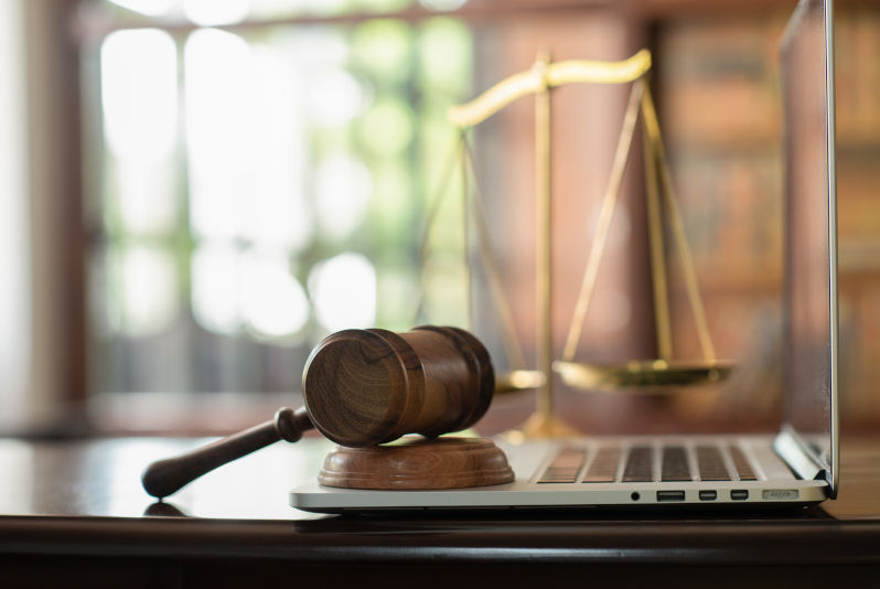 Judge gavel on computer with scales of justice on desk of lawyer.