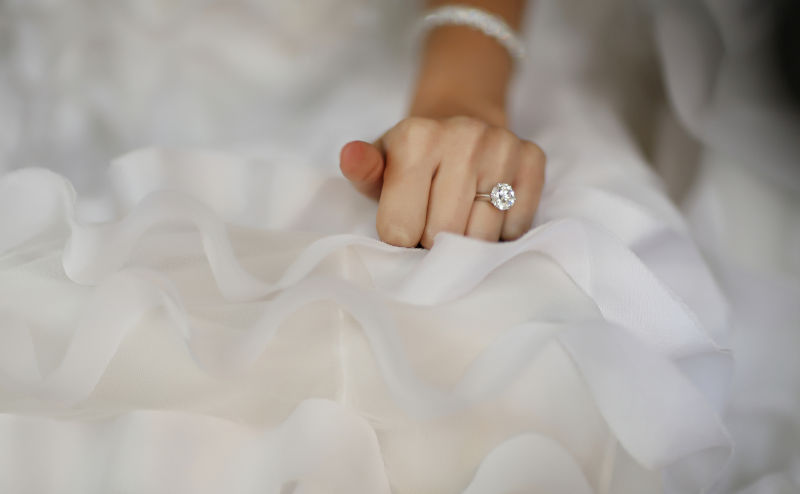 Bride's hand with beautiful diamond ring on white dress.