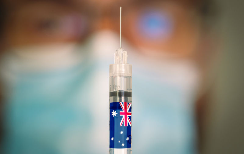 Close-up of hypodermic syringe with the flag of Australia and a blurred doctor on the background. Selective focus. Concept of Covid vaccination campaign in Australia