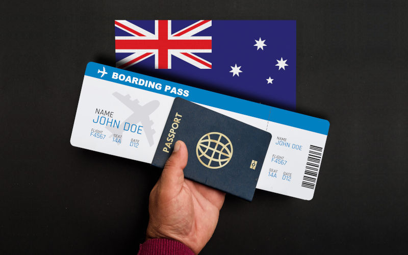 Hand holds passport and boarding pass with flag of Australia.