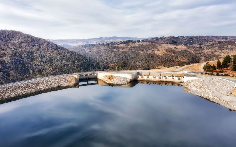 Huge concrete hydro energy dam on Snowy River forming JIndabyne lake - aerial view over shutter gate and road.