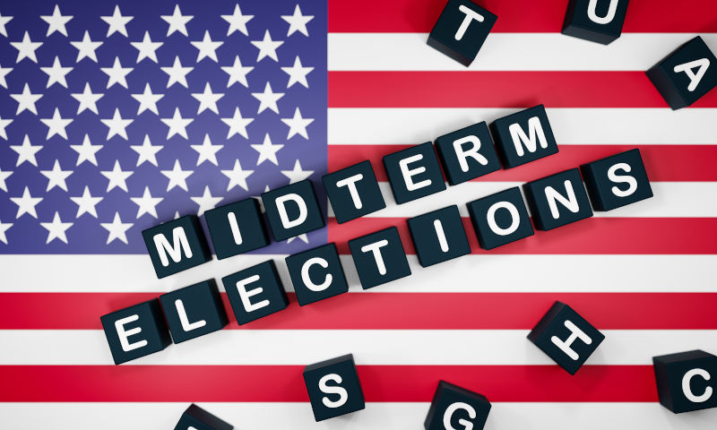 Black dices with the word midterm elections laying on a US American flag. US elections, voting and politics.