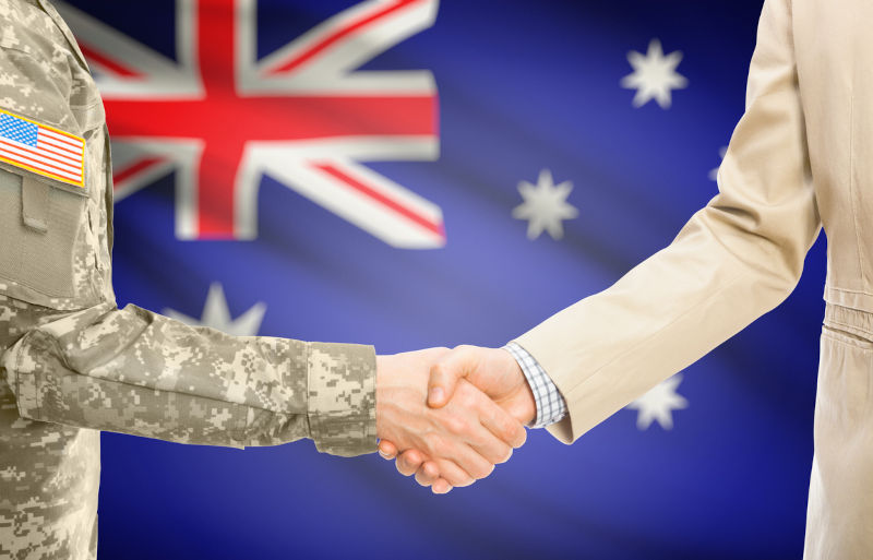 American soldier in uniform and civil man in suit shaking hands with Australian flag on background.