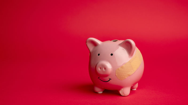 Broken piggy bank with beige adhesive on red background.