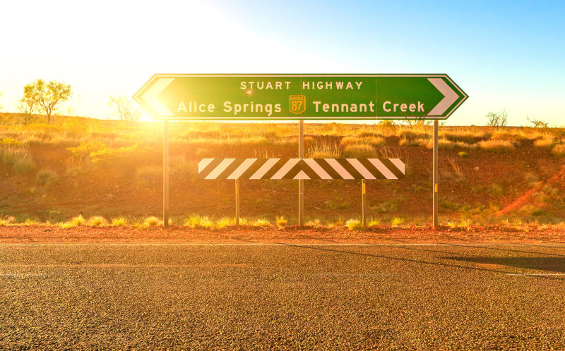 Northern Territory, Australia Outback. Stuart Highway signboard direction Alice Springs or Tennant Creek. Tourism in Central Australia, Red Centre. Sun with rays at sunset.