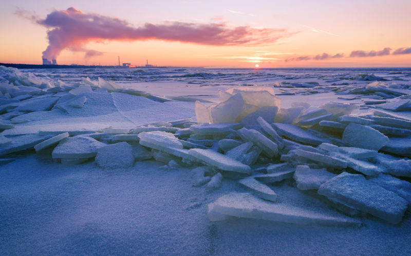 Nuclear power plant cooling tower in winter on snowy coast at sunset. Ice hummocks on winter frozen sea.