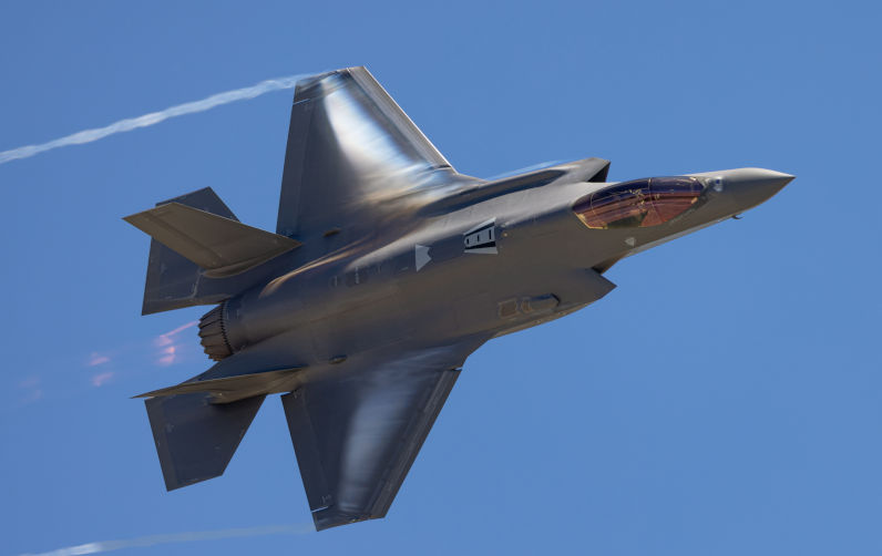 Very unusual close view of a F-35A Lightning II in a high G maneuver , with condensation clouds around the plane and afterburner on.