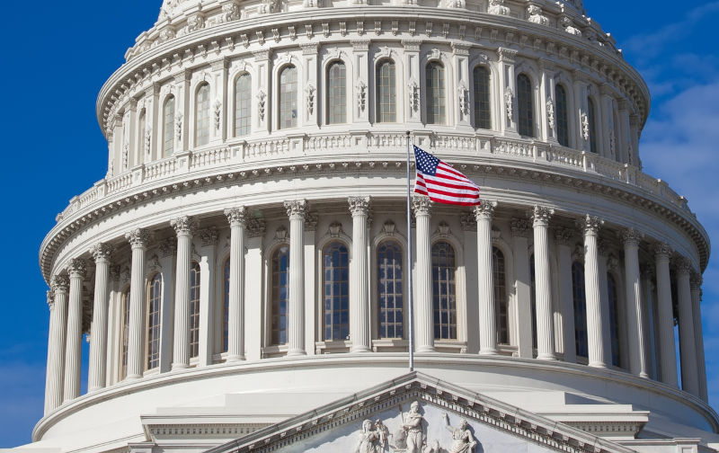 Capitol building close up Washington DC. The dome of American Capitol is on background at blue sky. In front of American flag.