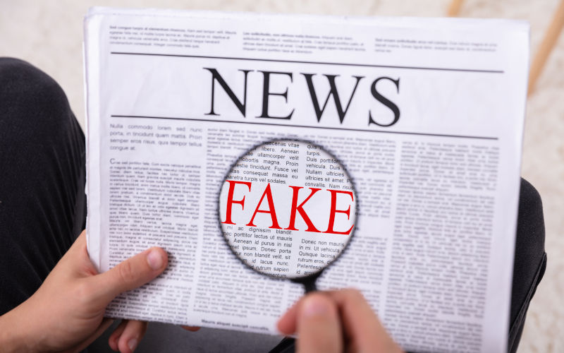 Man Examining Fake News On Newspaper Through Magnifying Glass