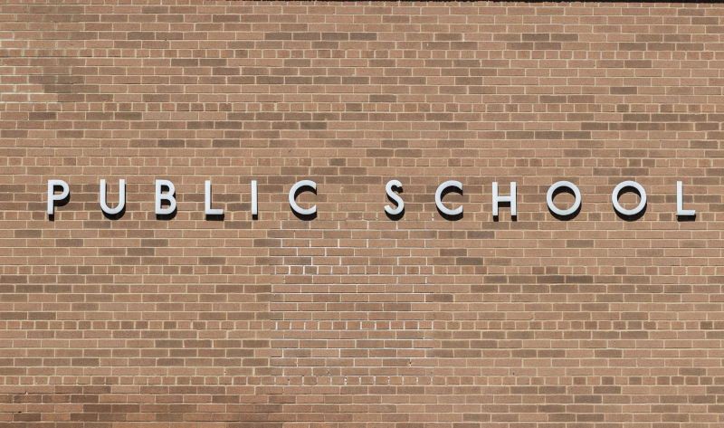 PUBLIC SCHOOL in stainless steel text against a brick background.