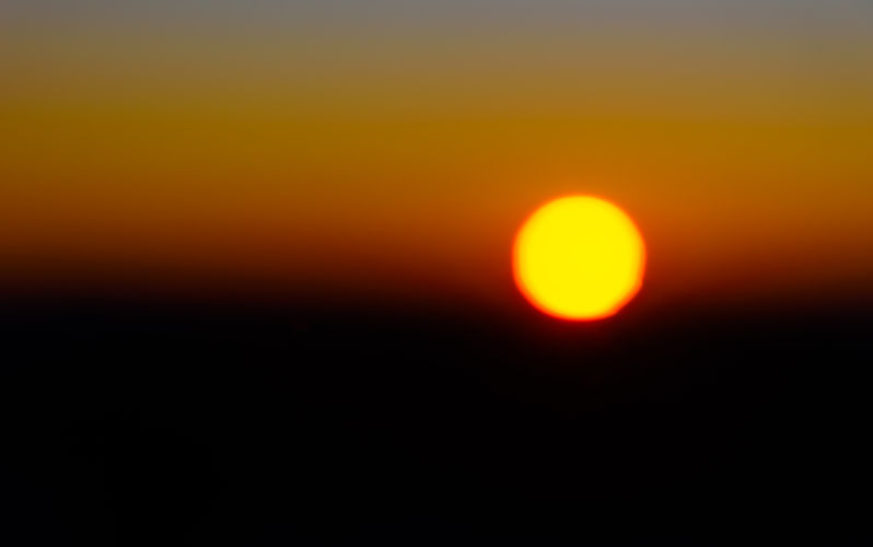 Sunrise in Australia; a dramatic contrast of red and black behind the gold disc of the sun; the image is reminiscent of the iconic Australian Aboriginal flag.