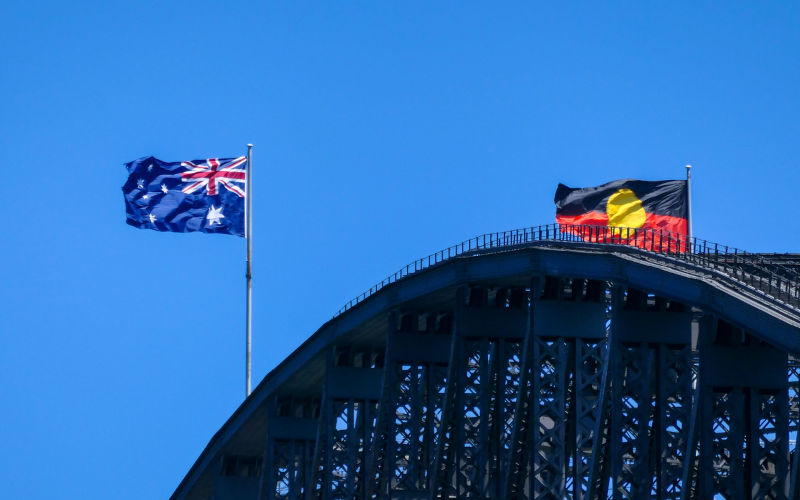 The Australian flag and Australian Aboriginal flag fly with a westerly wind on the Sydney Harbour Bridge on a Spring afternoon. This image was taken from Kirribilli on the eastern side of the bridge.