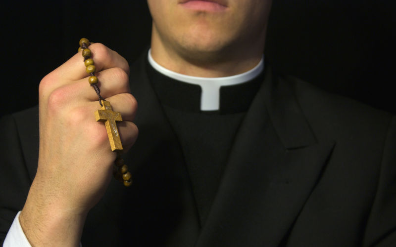 Young Priest praying with rosery in his hands