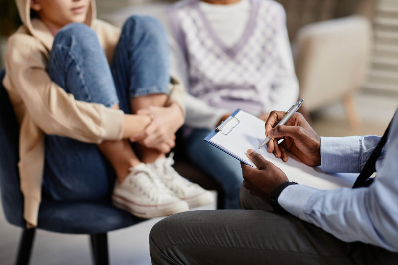 Psychologist taking notes on clipboard in therapy session for children.