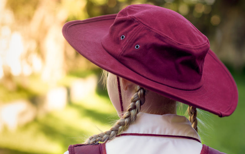 A girl wearing school uniform, white shirt, maroon backpack and maroon hat Back to school.