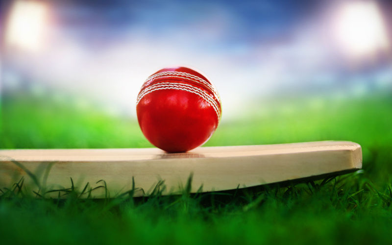 Cricket leather ball resting on bat on the stadium pitch bright stadium lights projecting on red leather ball.