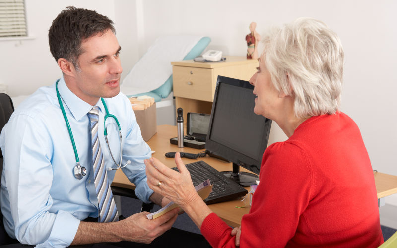 GP talking to senior woman in surgery sitting down looking at each other.