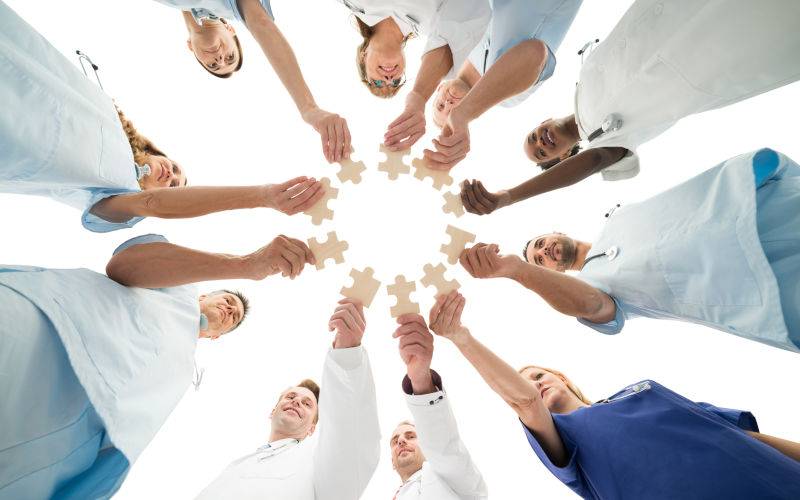 Directly below shot of medical team joining jigsaw pieces in huddle against white background