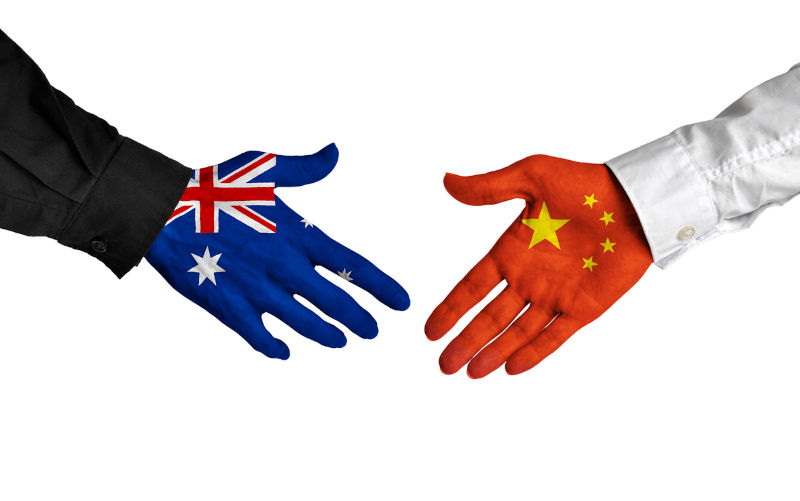 Diplomatic handshake between leaders from Australia and China with flag-painted hands.