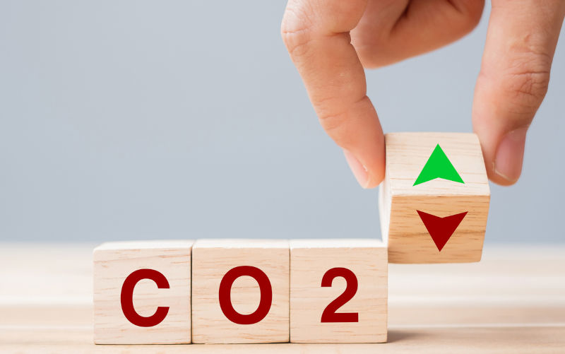 Hand flipping wooden cube blocks to UP and Down arrow symbol with CO2 (Carbon dioxide) text on table background. Free Carbon, alternative energy and global climate change concepts