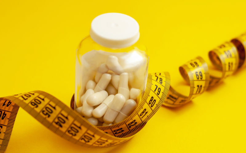 Tablets in capsules in a glass jar, tied with measuring tape on a yellow background.