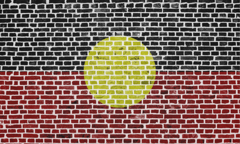 Close-up on a brick wall with the flag of Australian Aboriginal painted on it. Image: iStock