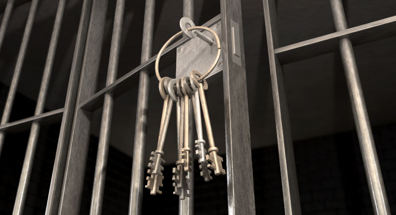 A closeup of the lock of a jail cell with iron bars and a bunch of key in the locking mechanism with the door open.