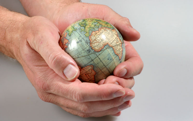 Man's hand cradling a vintage globe.