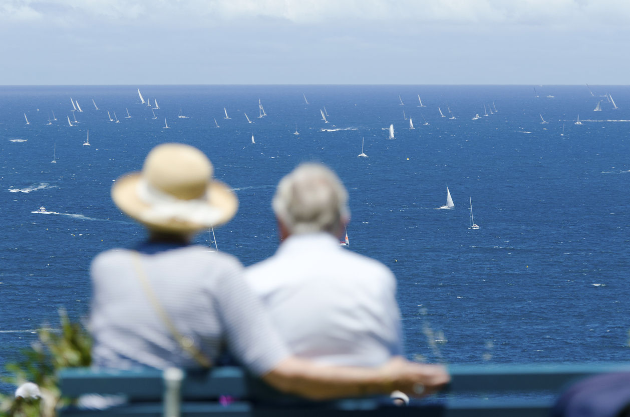 People Sitting on Benches Near Ocean Watching Yacht Race.