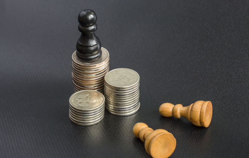 money concept. Black wooden chess pawn standing on coins, two white pawn fell, bowed