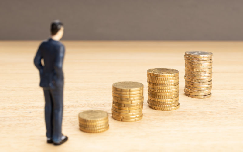 Businessman figurine looking at the growth of stacked coins. Saving money for finance accounting.