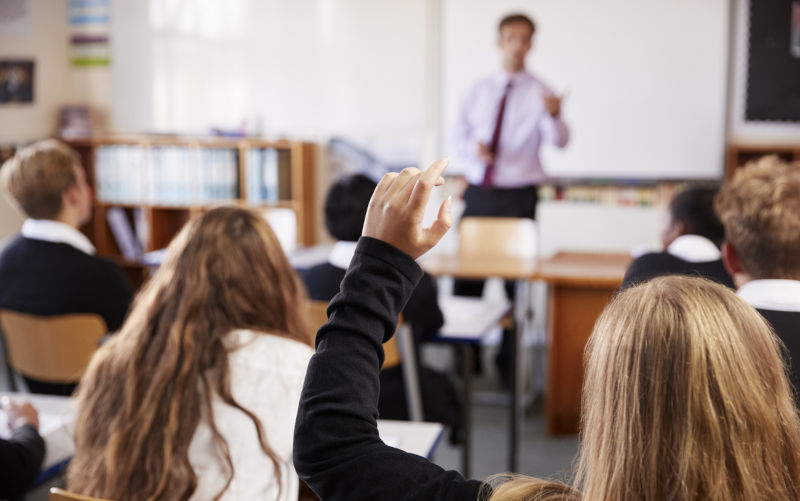 Female Student Raising Hand To Ask Question In Classroom.