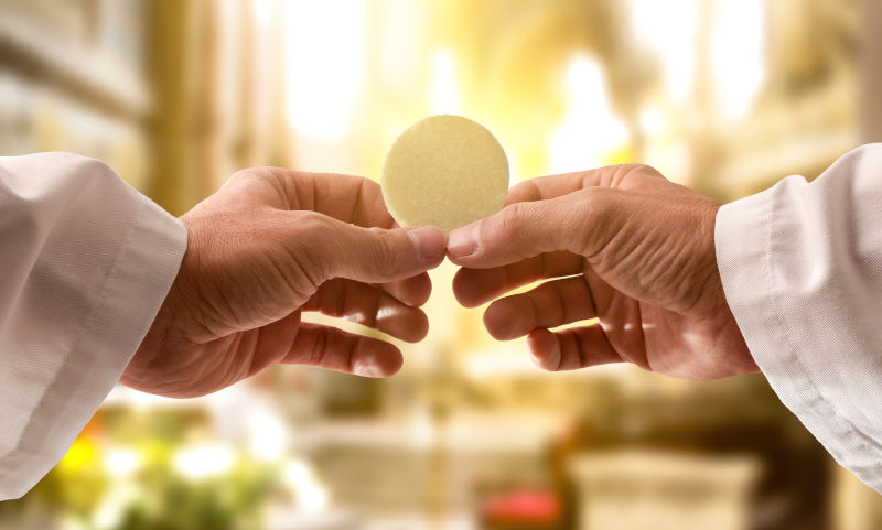 Hands of a priest consecrating a host as the body of Christ to distribute it to the communicants in the church.