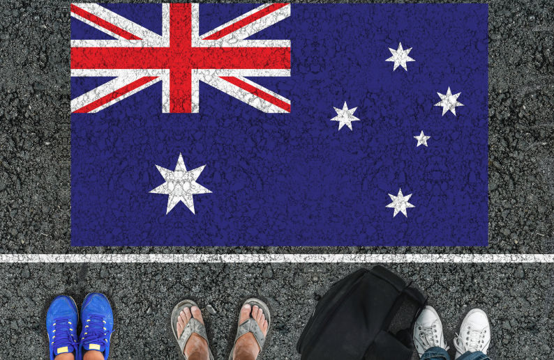 People legs are standing on asphalt road next to flag of Australia and border.