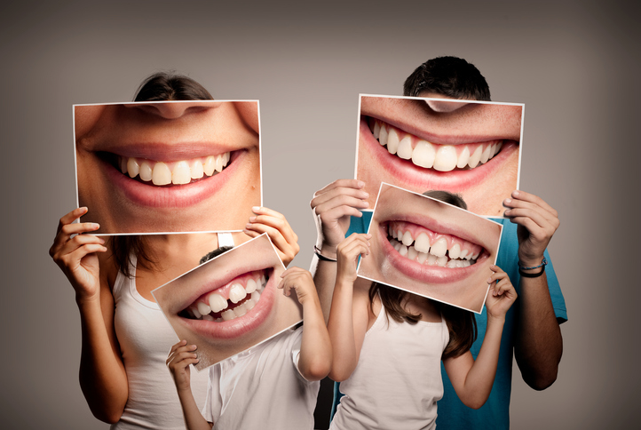 Family of four, two adults and two children holding up images to symbolise dental care Image: iStock